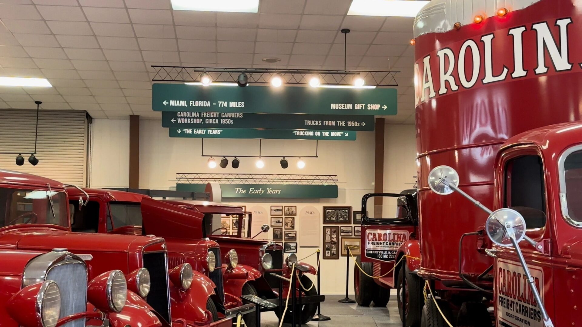 An indoor exhibit featuring vintage red trucks and signage pointing towards various locations and historical periods, including Miami, Florida, and the Great Smokey Mountains National Park.