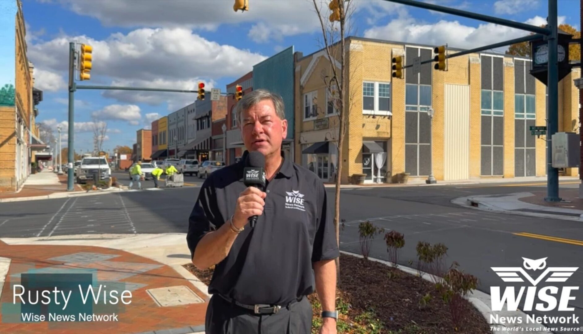 A man standing on the side of a road holding a microphone.