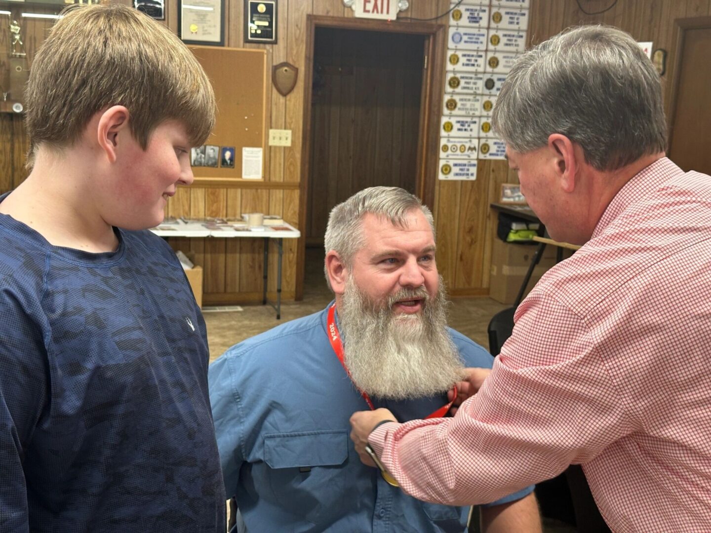 A man with long white beard is getting his hair cut by two men.