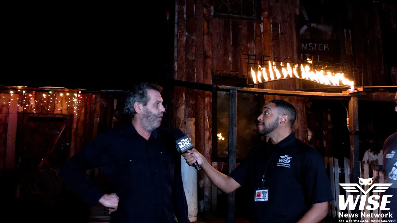 A man with a microphone interviews another man in front of a rustic building at night, with "WISE News Network" displayed on the microphone.