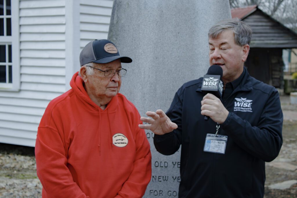 Two men, one in a red hoodie marked with " The Cherryville New Years Shooters" and another in a black Jacket Marked with Wise News Network. 