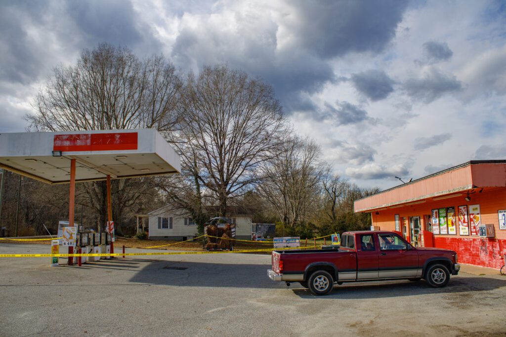 A bright orange convenience store with a gas pump station outside it surrounded by caution tape. The canopy of the pump station is leaning slightly. 