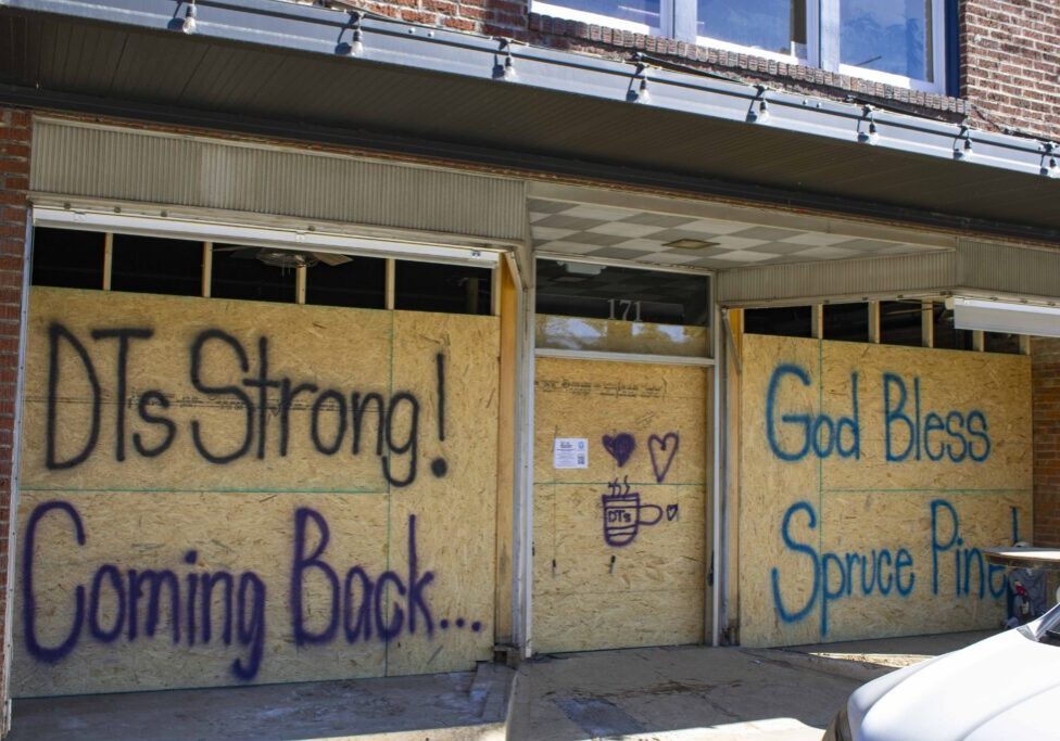 An image of DT's Blue Ridge Java being boarded up after flood damages with hopeful messages such as DT's Strong, Coming Back!, and God Bless Spruce Pine painted on it.