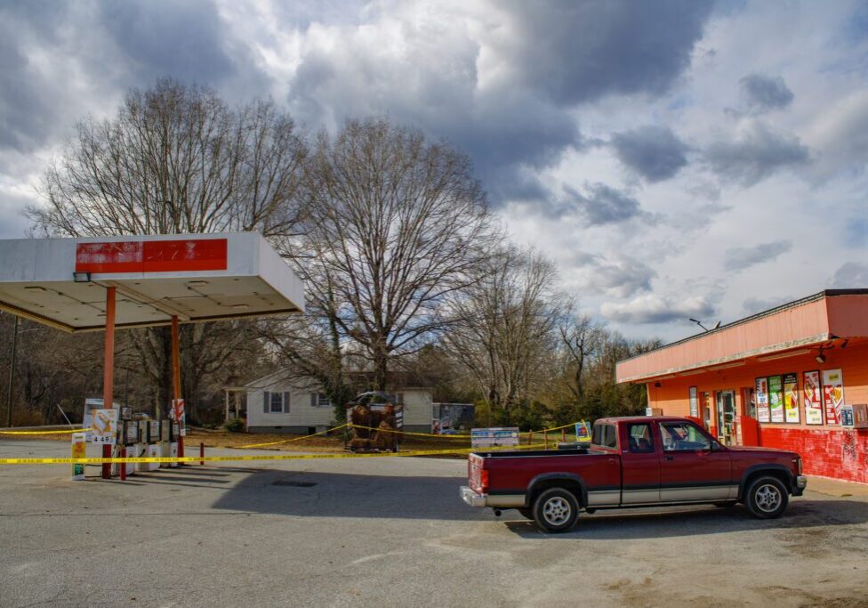 A bright orange convenience store with a gas pump station outside it surrounded by caution tape. The canopy of the pump station is leaning slightly.