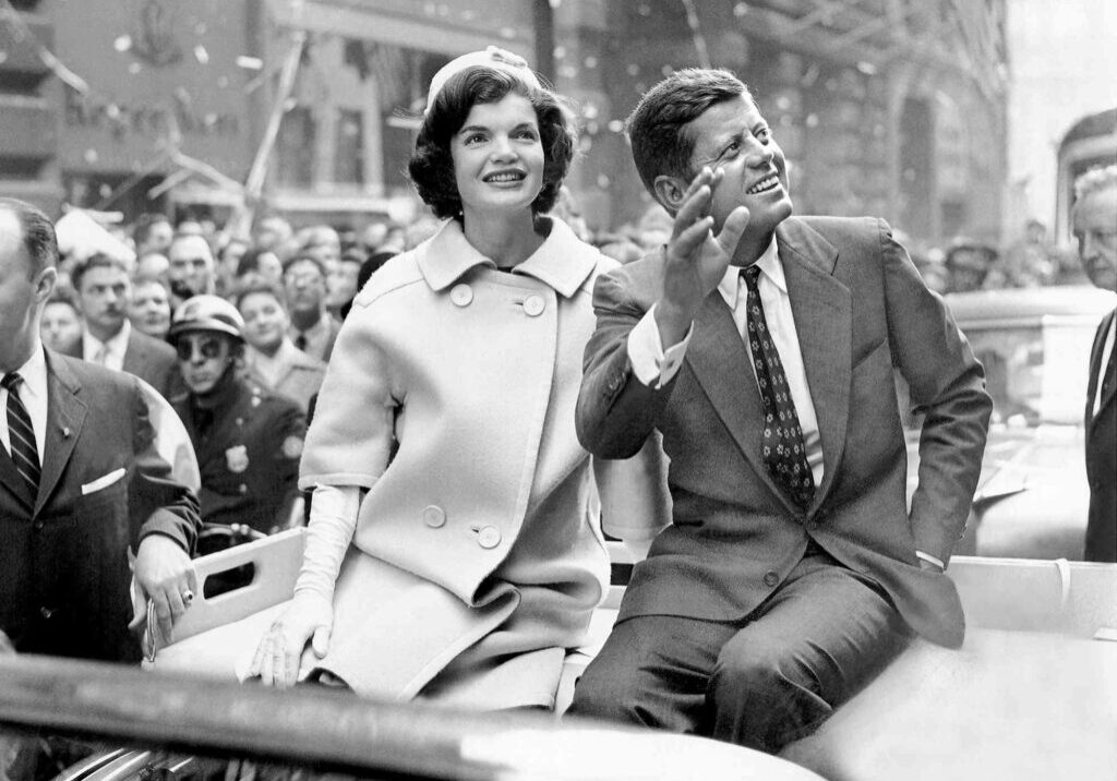 President John F Kennedy and his wife riding in a parade.