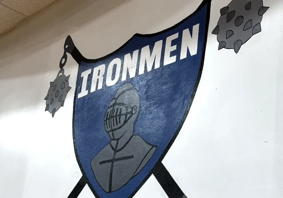 A wall mural features a blue and gray shield with the word "IRONMEN" and a knight's helmet. The shield is flanked by two spiked maces.