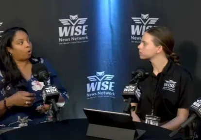 Four people in a panel discussion at a table with microphones, under WISE News Network banners.