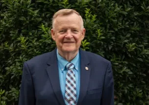 A man in a suit and tie standing next to a bush.