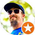 A person with a beard, wearing a cap and sunglasses, is seen outdoors. A star-shaped icon is overlayed on the image's lower right corner.